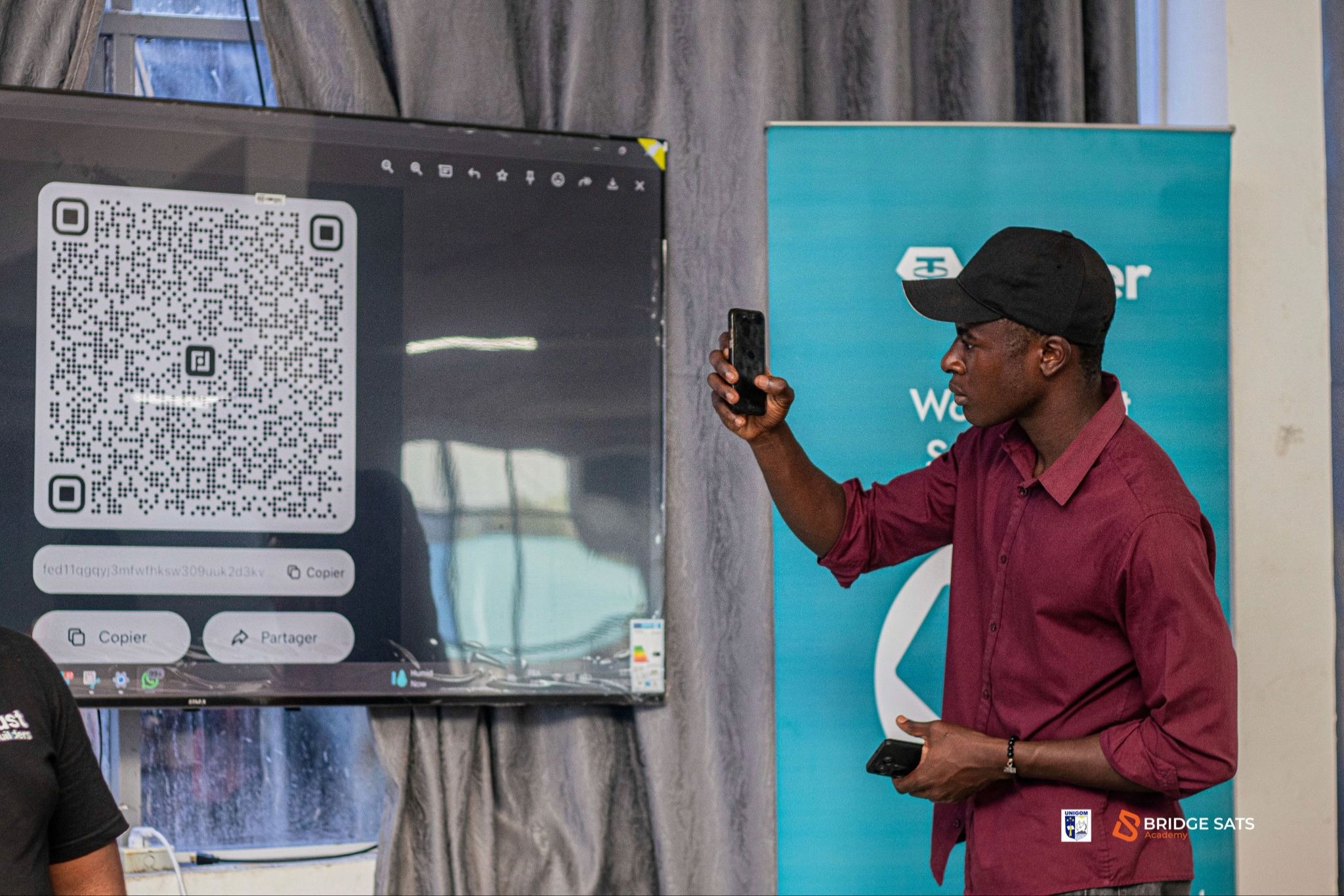 Bridge Sats presenter demonstrating a Fedi Bitcoin wallet QR code payment at a community event in the DRC