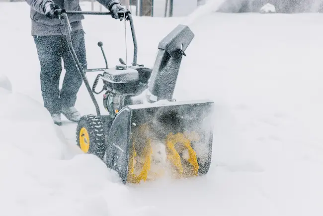worker with snowblower clearing snow from sidewalk
