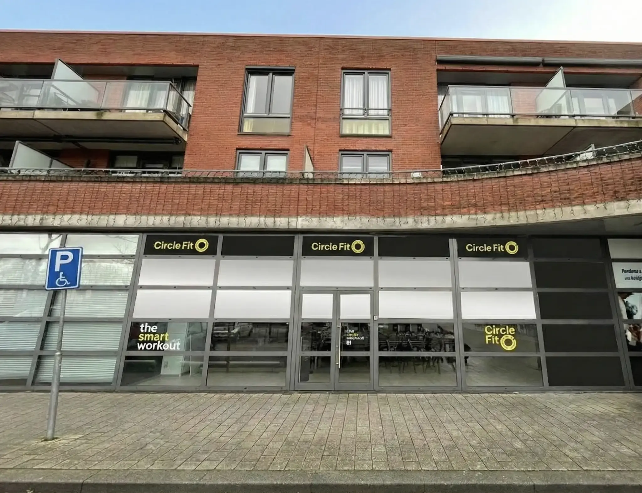 A Circle Fit with large windows featuring yellow signs and an entrance door, with customers visible inside.