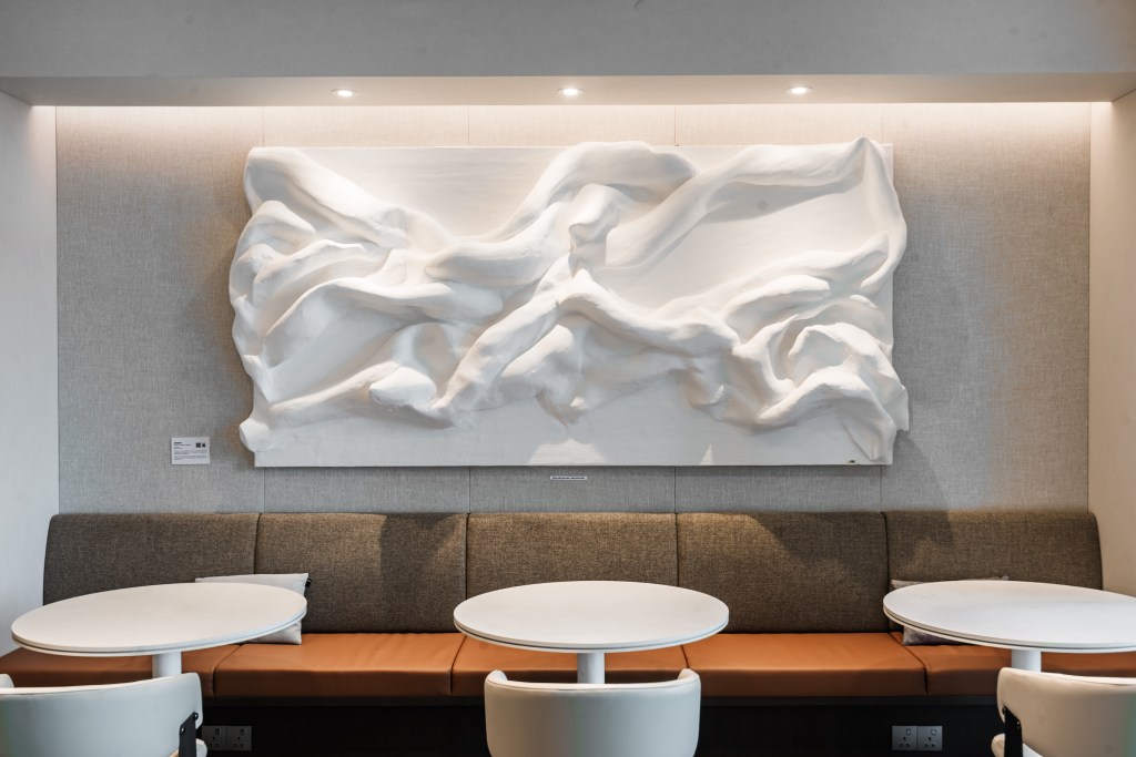 Artistic white wall sculpture above a cozy seating area with round tables in a modern coworking space