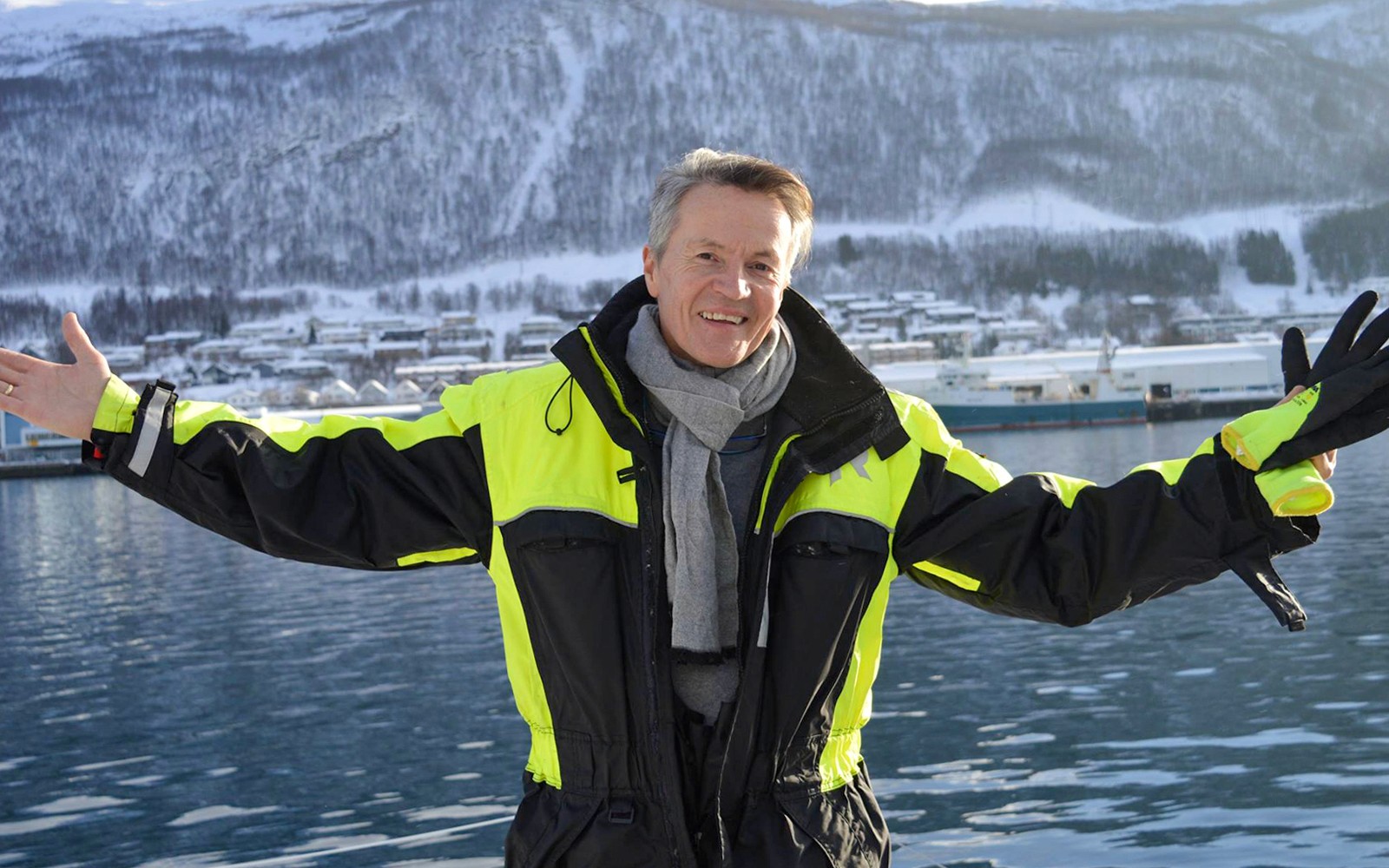 Guest in thermal suit on a cruise with snowy mountains in the background.
