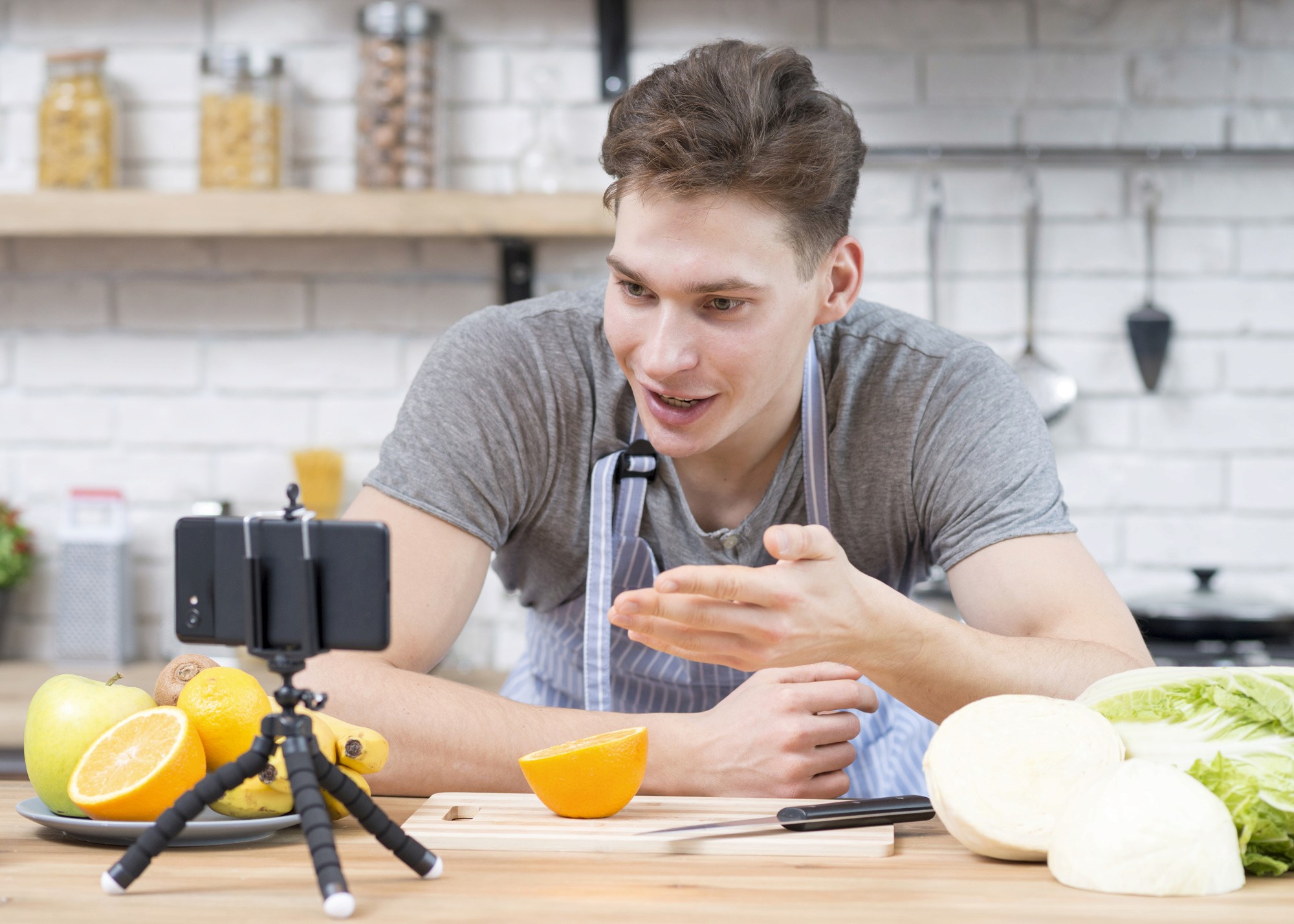 A man holds an orange while capturing a photo with his smartphone, showcasing a moment of enjoyment and creativity.