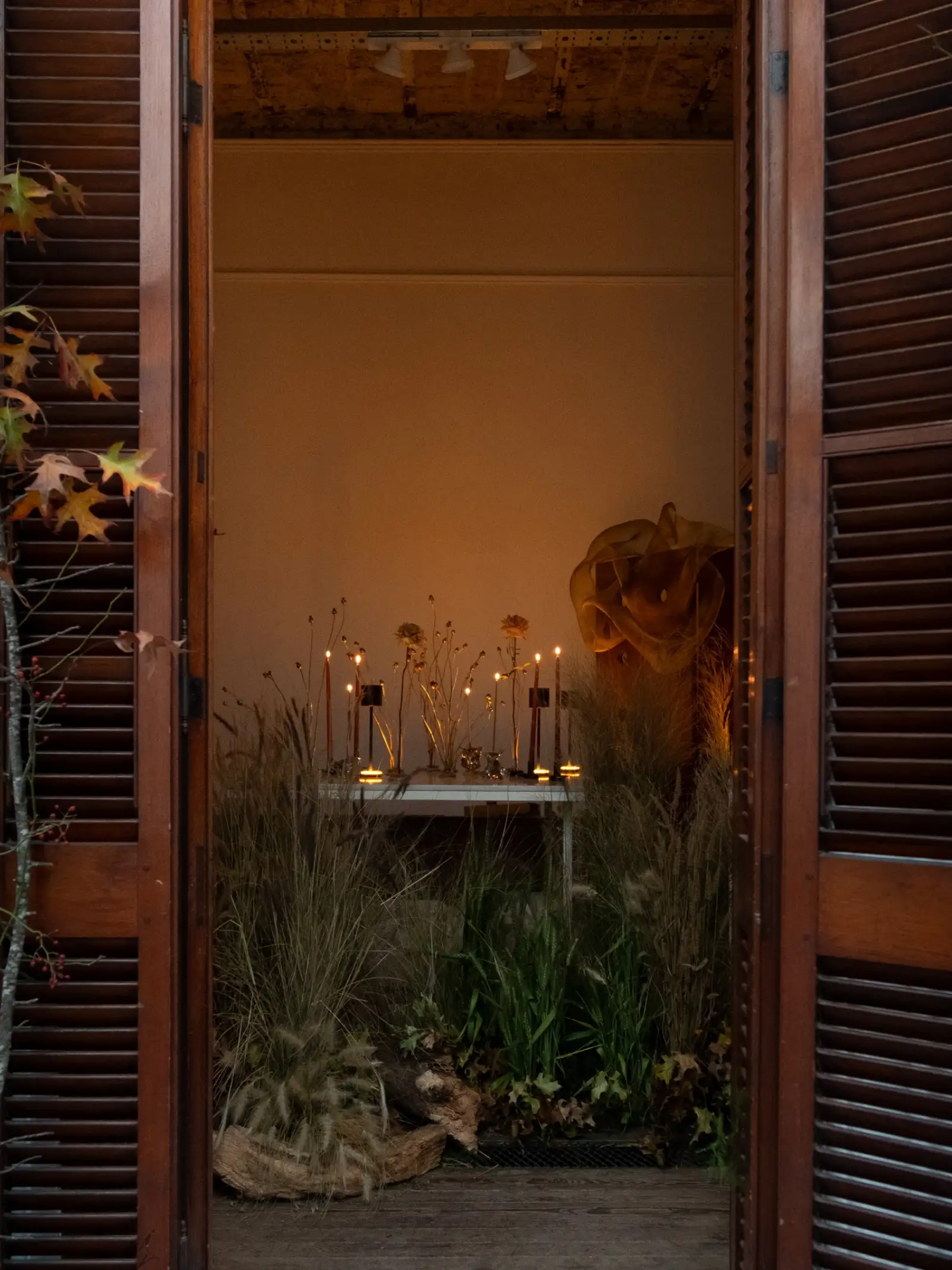 Escenografía botánica con velas y follaje seco para instalación artística, transmitiendo un clima íntimo y ritual.