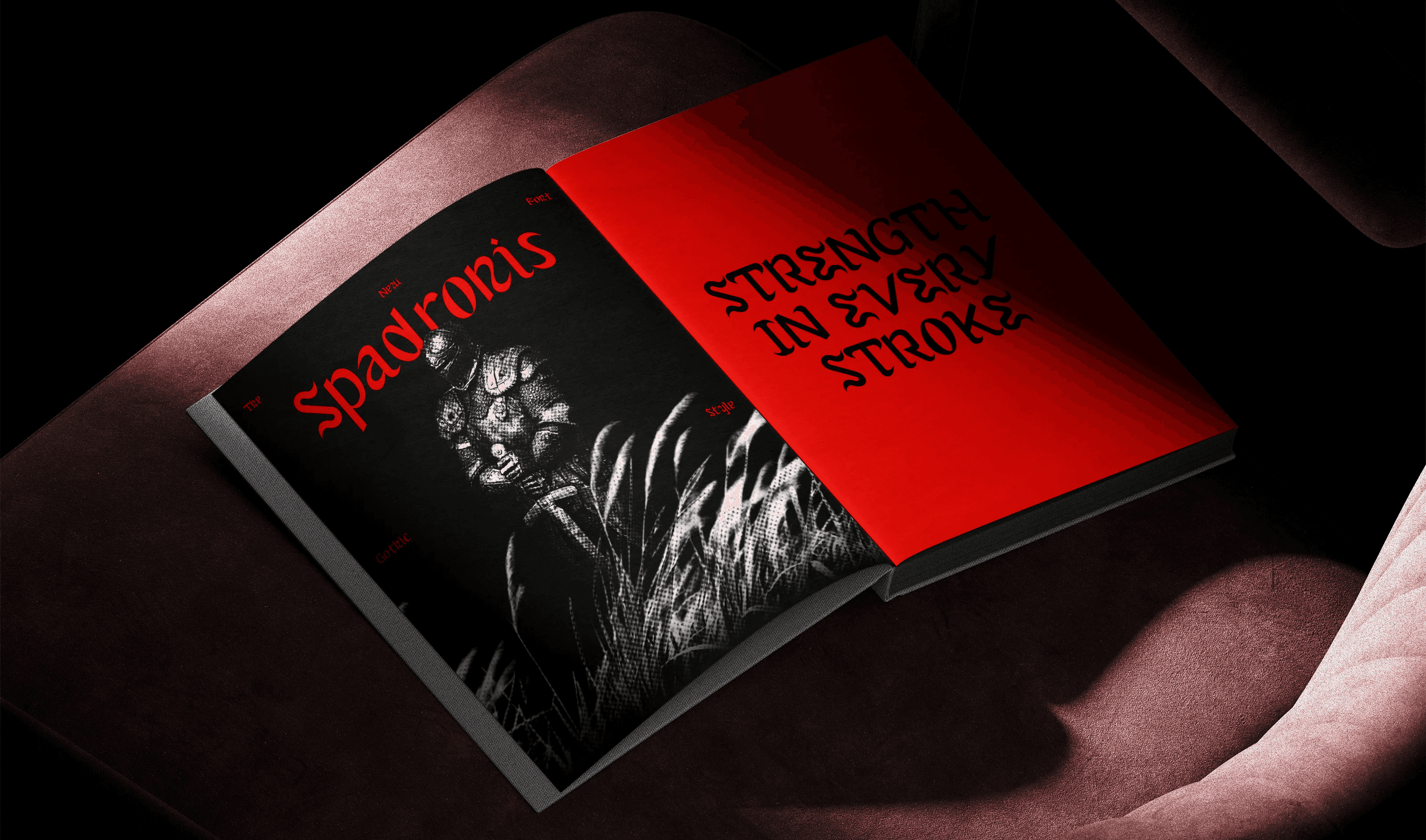 Un livre ouvert à la couverture sombre et rouge est posé sur un fauteuil. On y lit notamment « Spadronis » et « Strength in every stroke .
