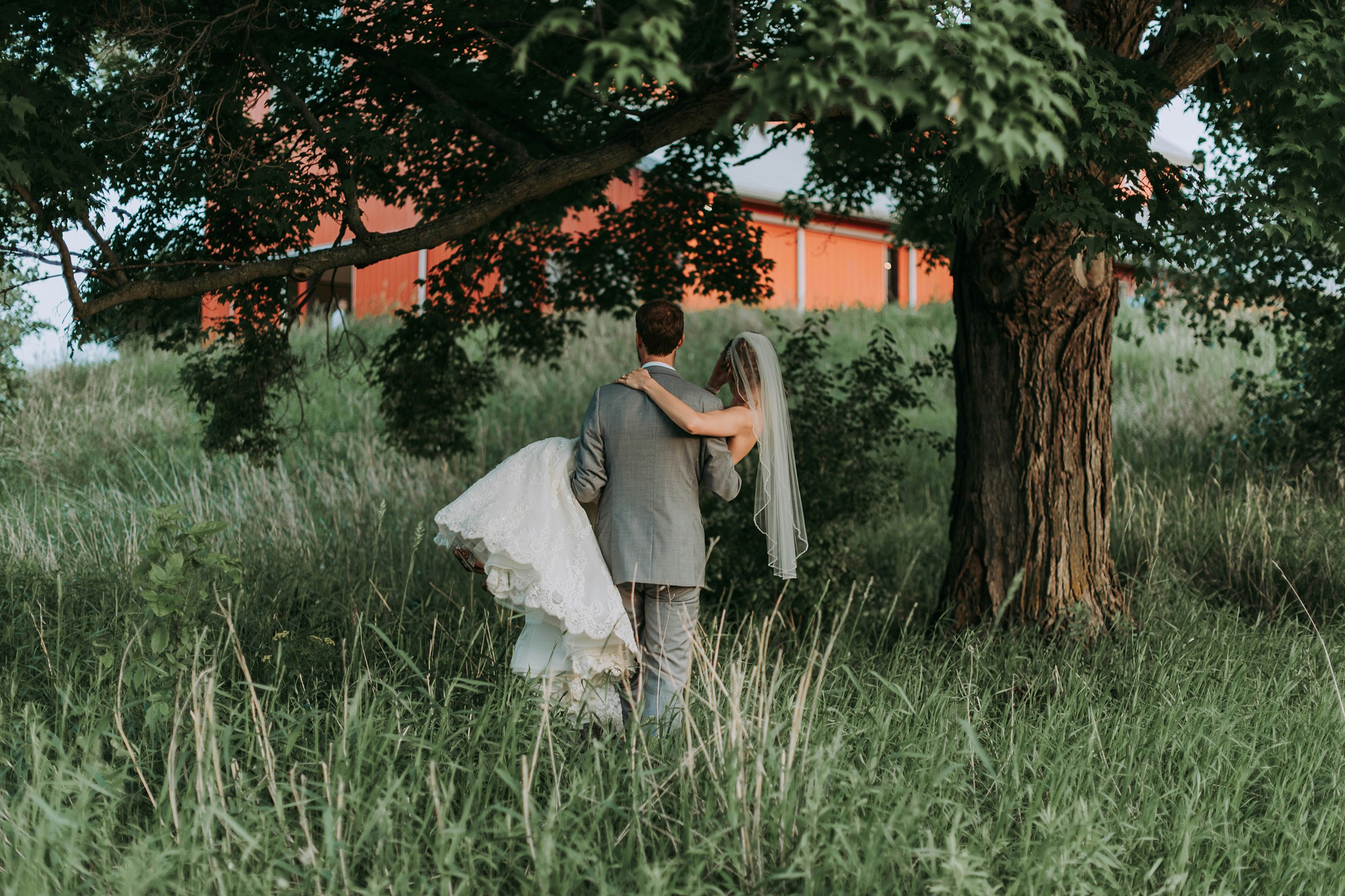 A groom in a gray suit carries his bride.