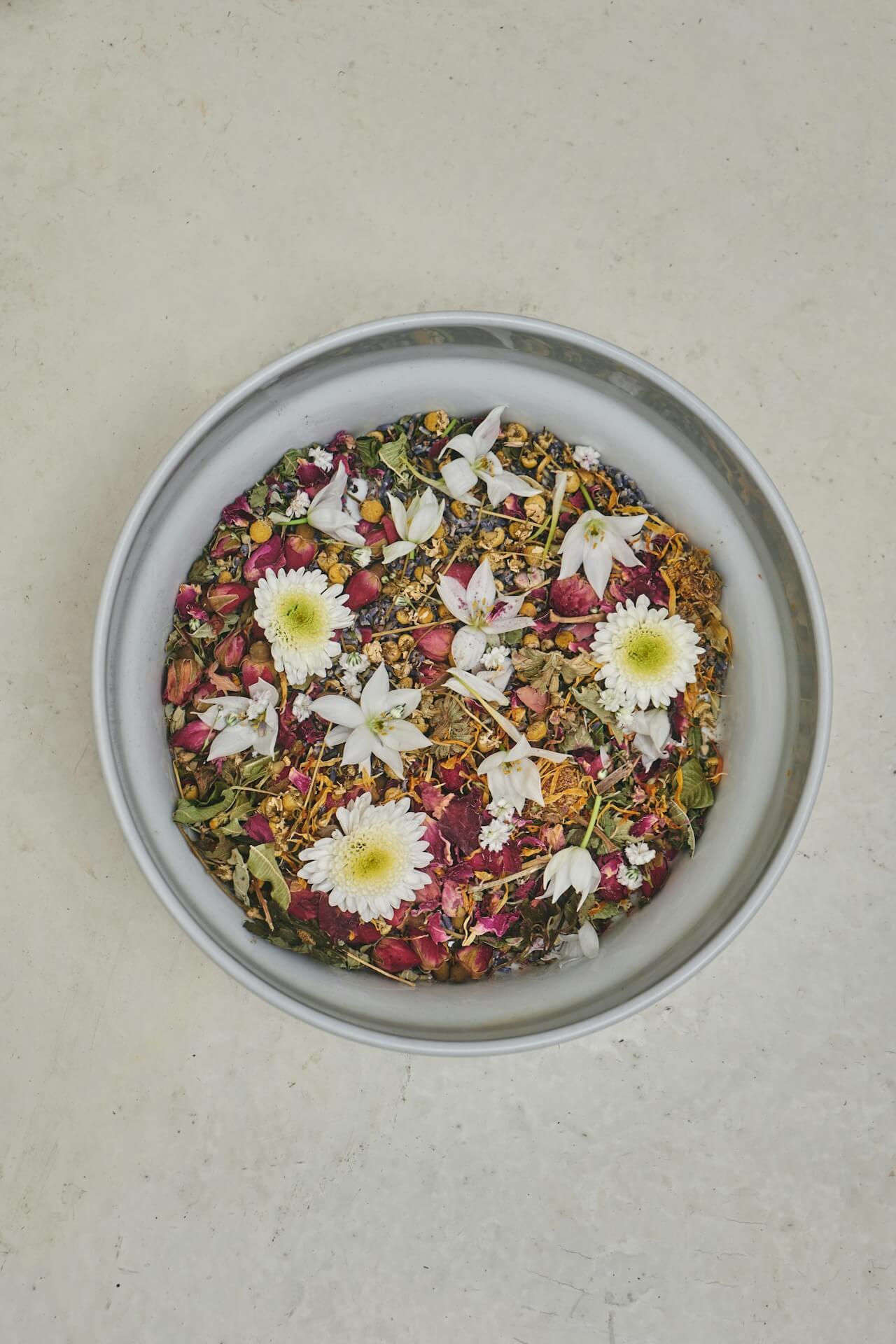Overhead shot of a bowl containing a mix of different fresh and dried herbs sitting on top of a beige countertop