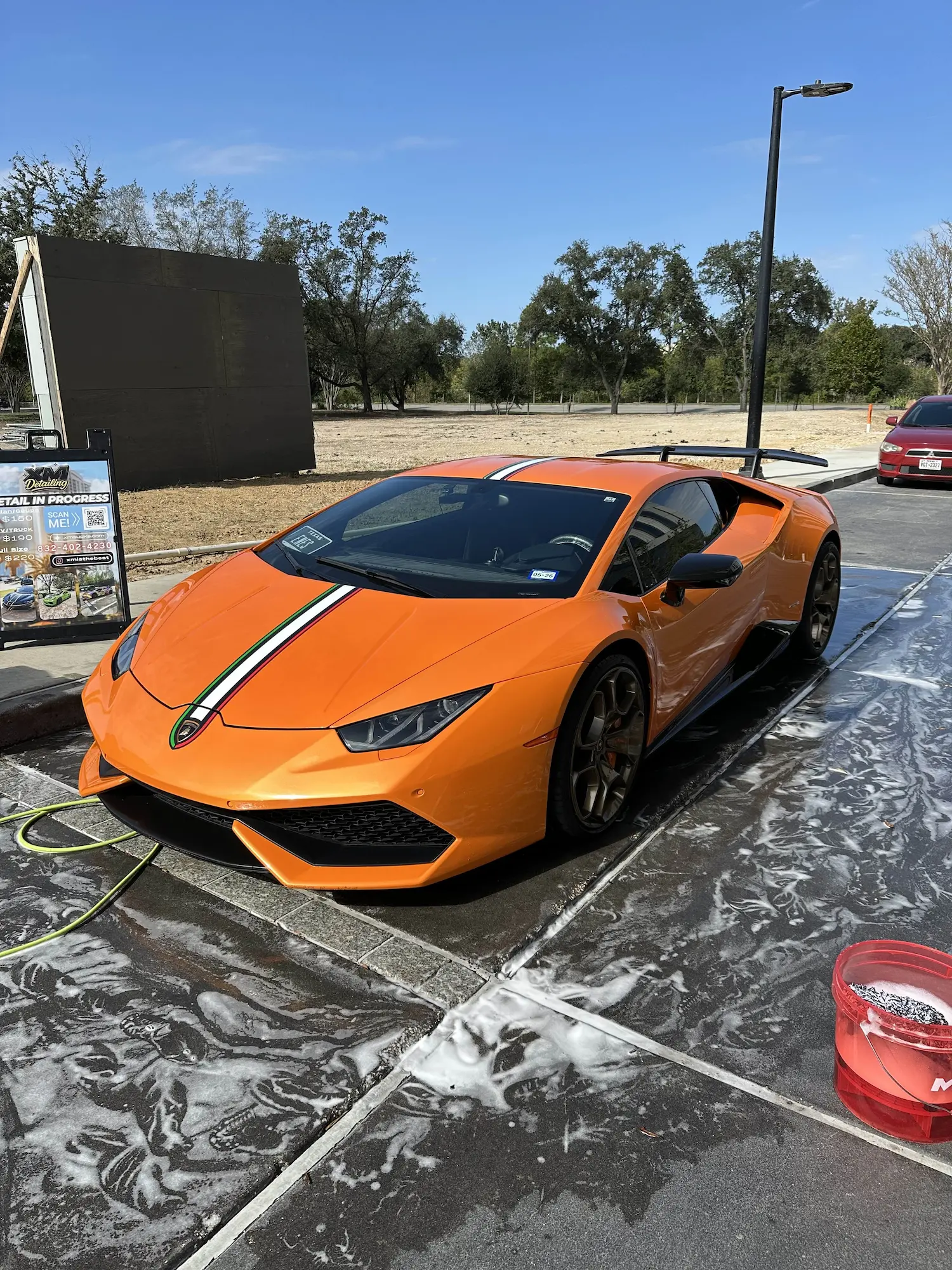 An orange Lamborghini Huracán with Italian flag stripes undergoing a professional hand wash and foam bath at a Houston mobile detailing station.