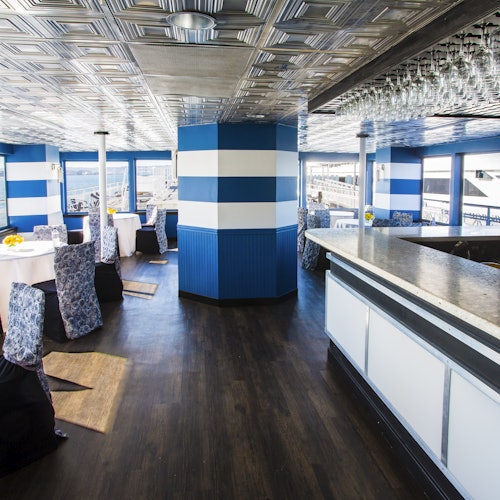 Un restaurante iluminado con paredes de rayas azules y blancas, sillas con patrones, y una barra, con vistas al océano afuera.