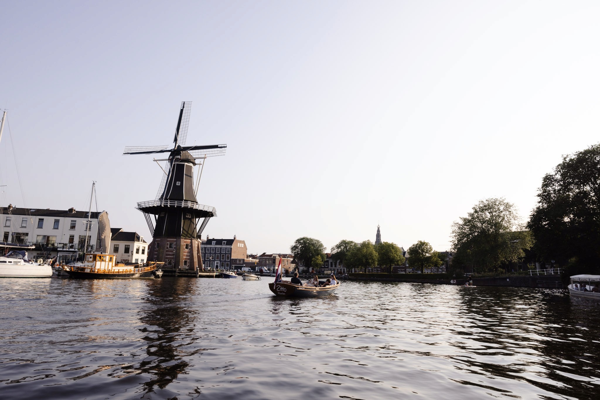 Fotografie van een historische molen in Haarlem, reflecterend in het kalme water, met een serene landelijke omgeving op de achtergrond