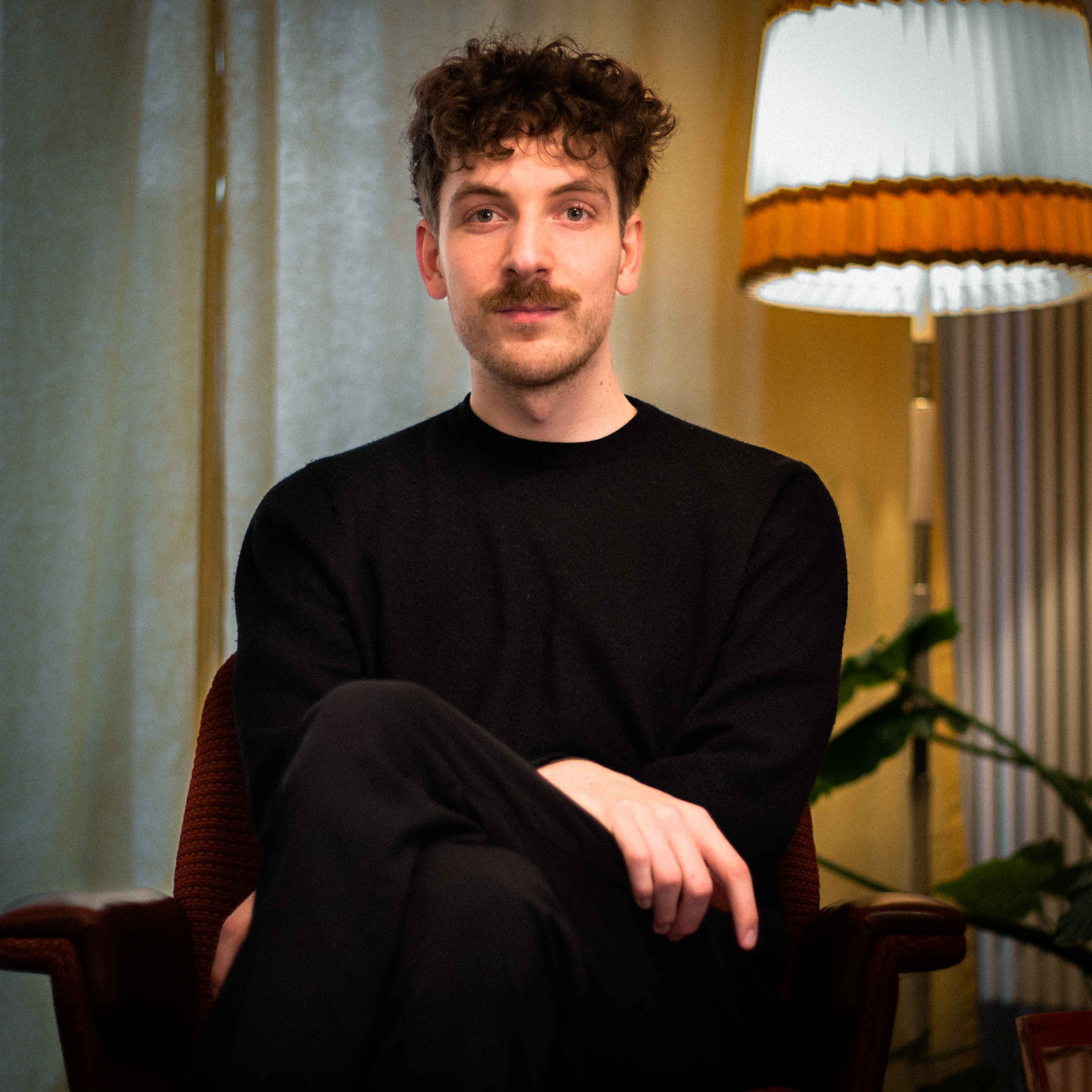 Theo Weise sitzt vor einer Orange/Weißen Lampe (Portrait)