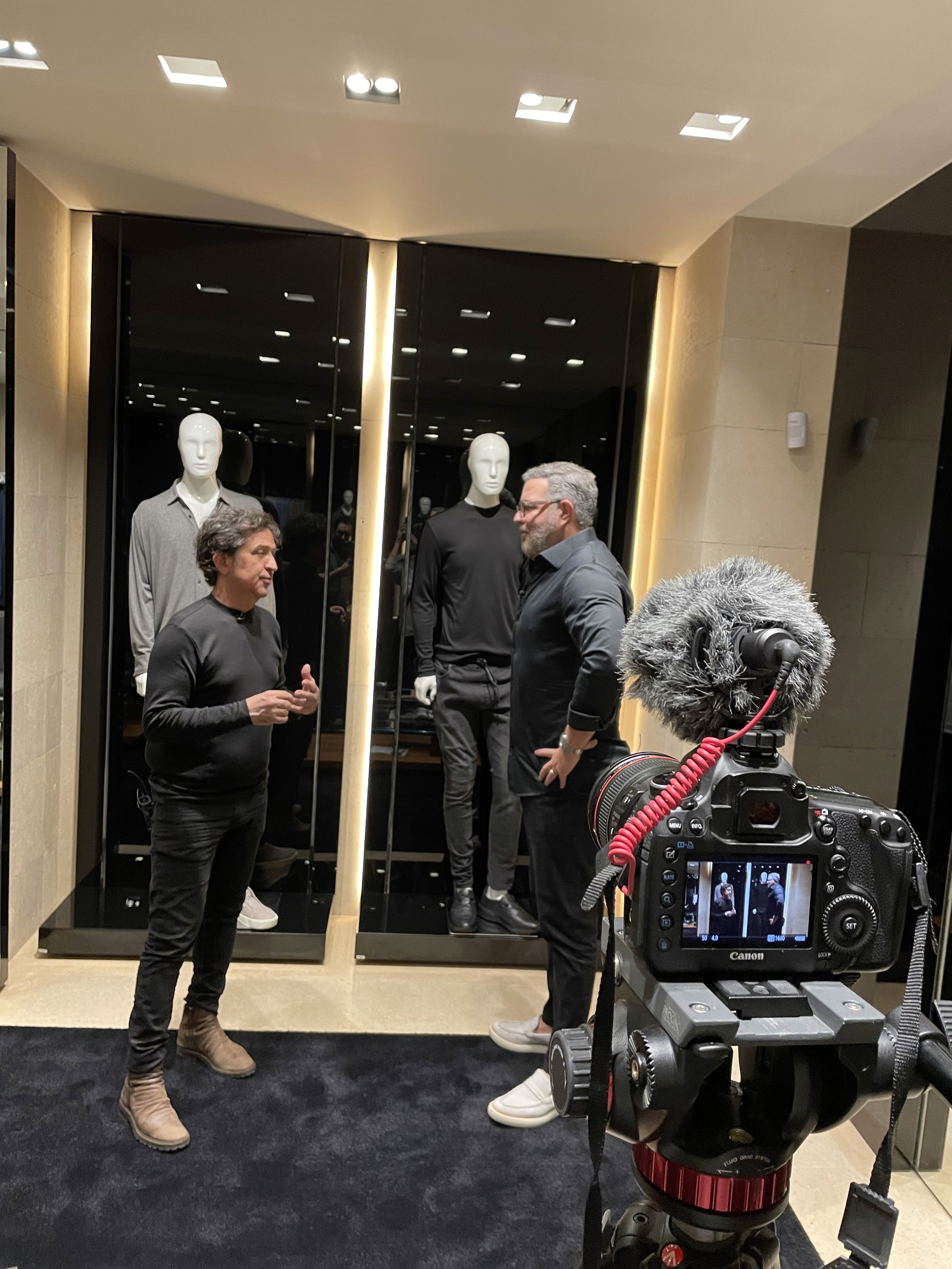 A smiling young man with crossed arms, wearing a plaid shirt and white t-shirt, poses against a dark background.