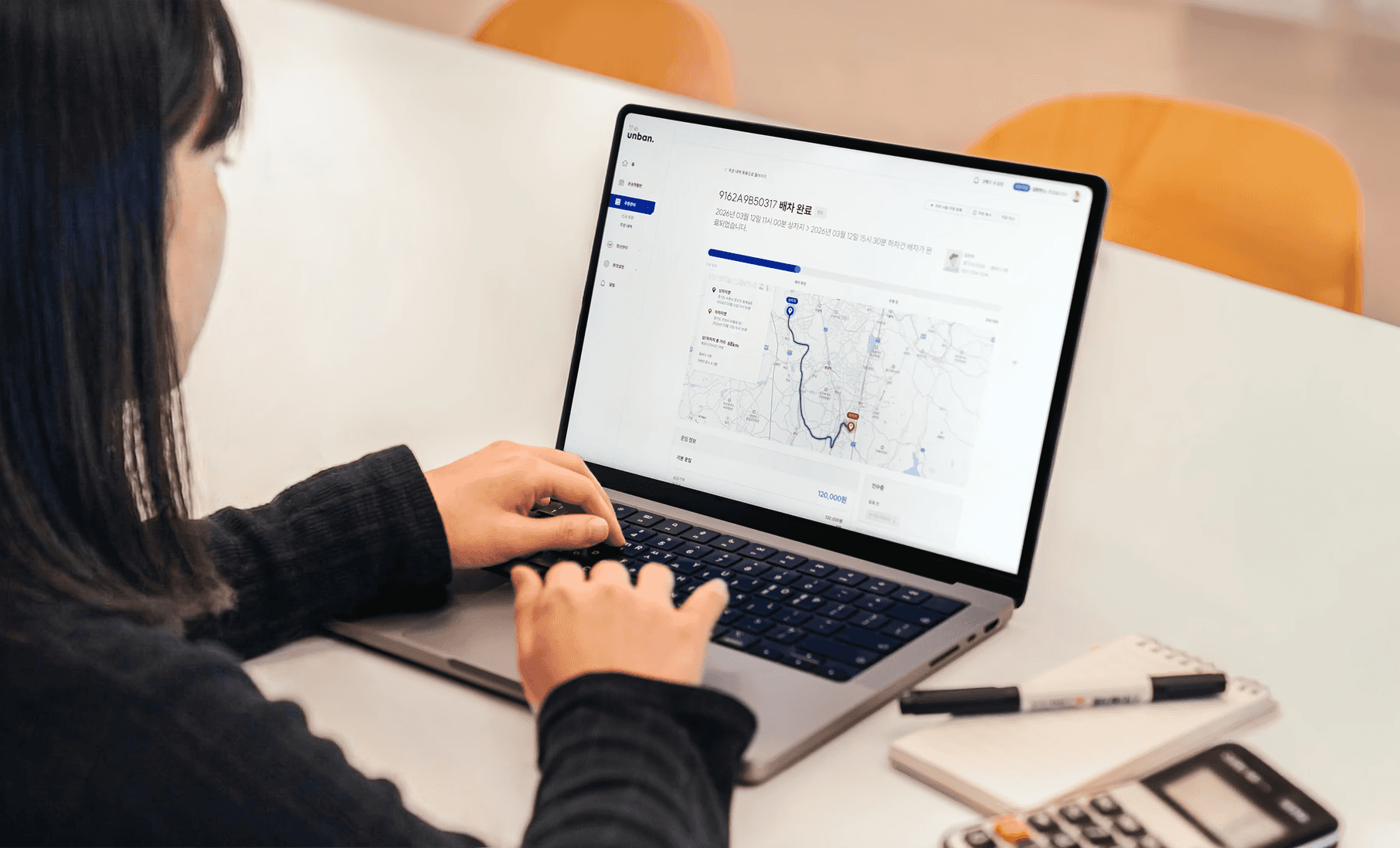 CJ대한통운 더 운반 바로주문 서비스를 소개하는 히어로 이미지로, 노트북 화면에 배차 완료 상태의 운송 경로 지도와 운임 정보가 표시되어 있습니다. AI가 산출하는 최적 운임으로 전국 차주 매칭과 실시간 관제까지 한 번에 처리할 수 있음을 안내합니다.
