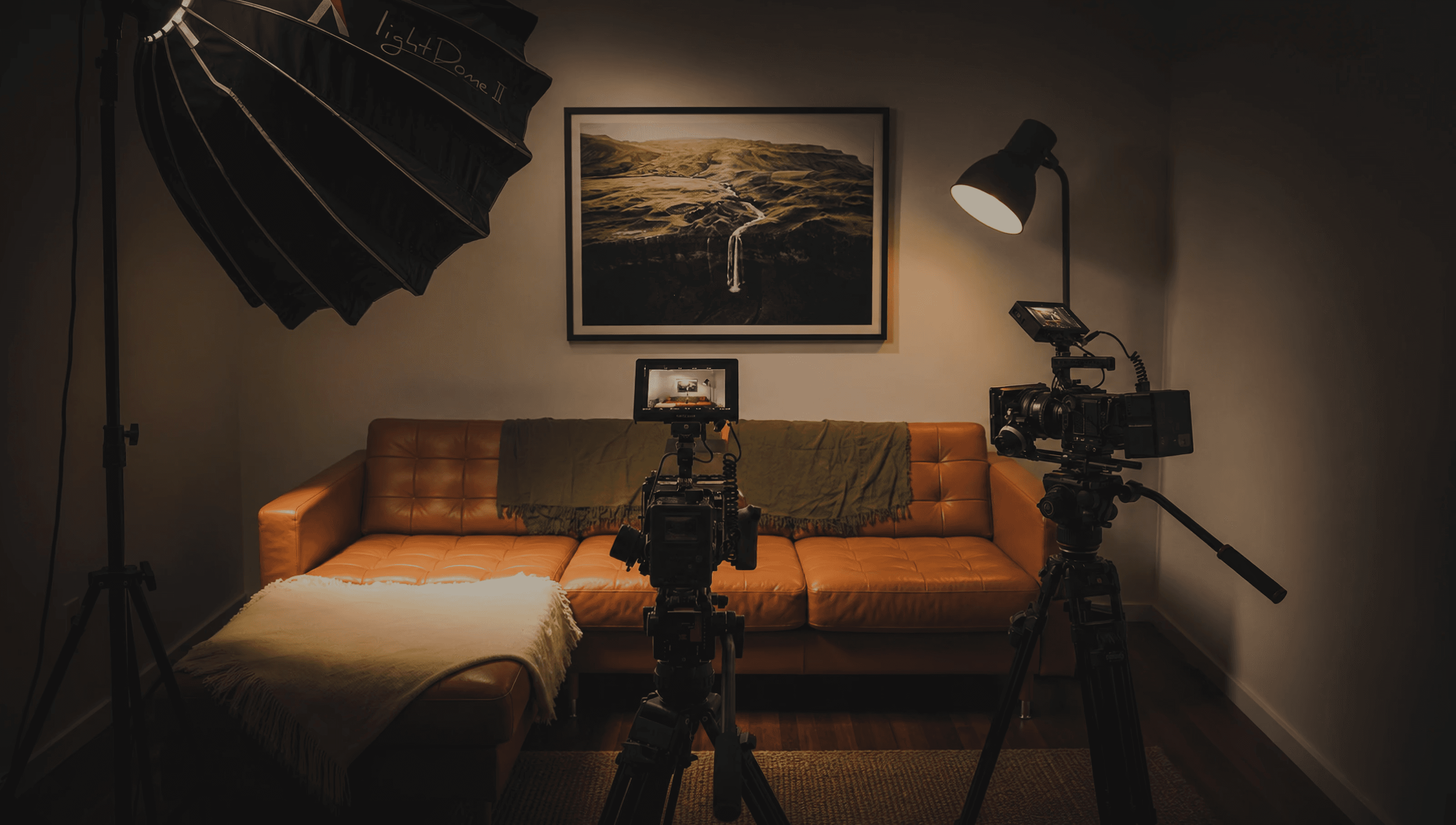 Interview set lit indoors, with two cameras on tripods facing a sofa and a softbox off to one side