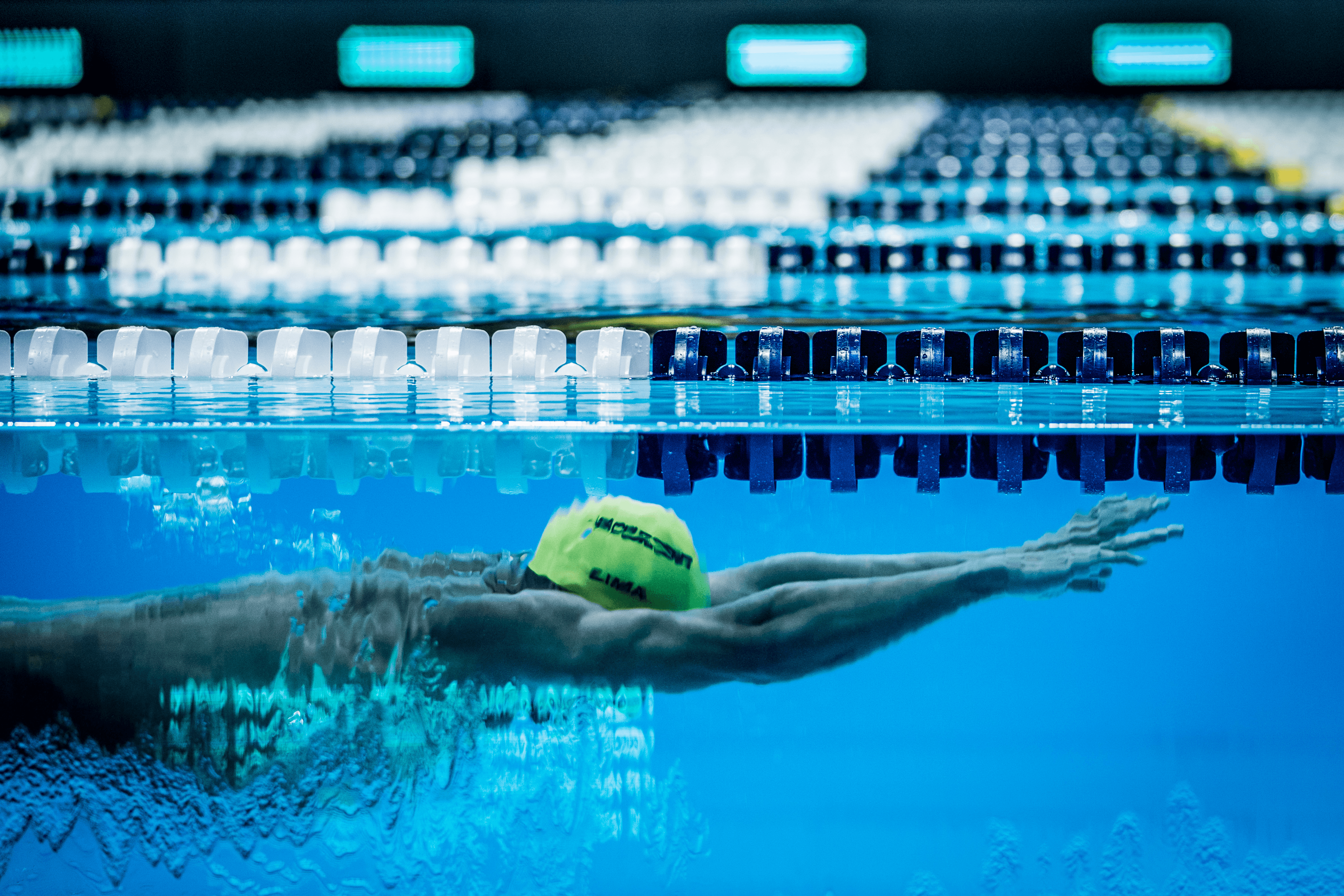 swimmer diving underwater, seen through a glass pool wall