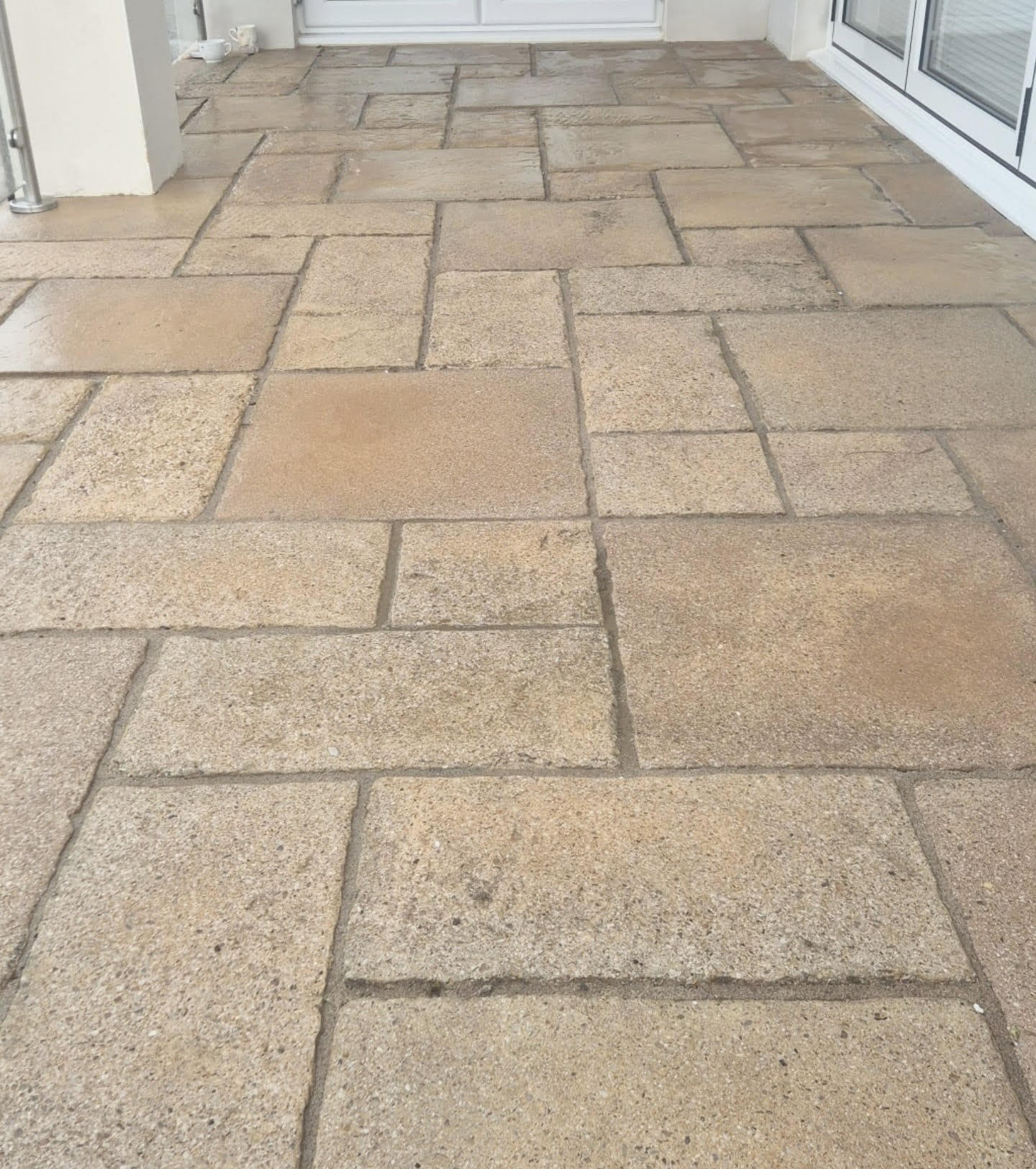 Beige textured stone tiles arranged in a grid pattern cover a patio area.