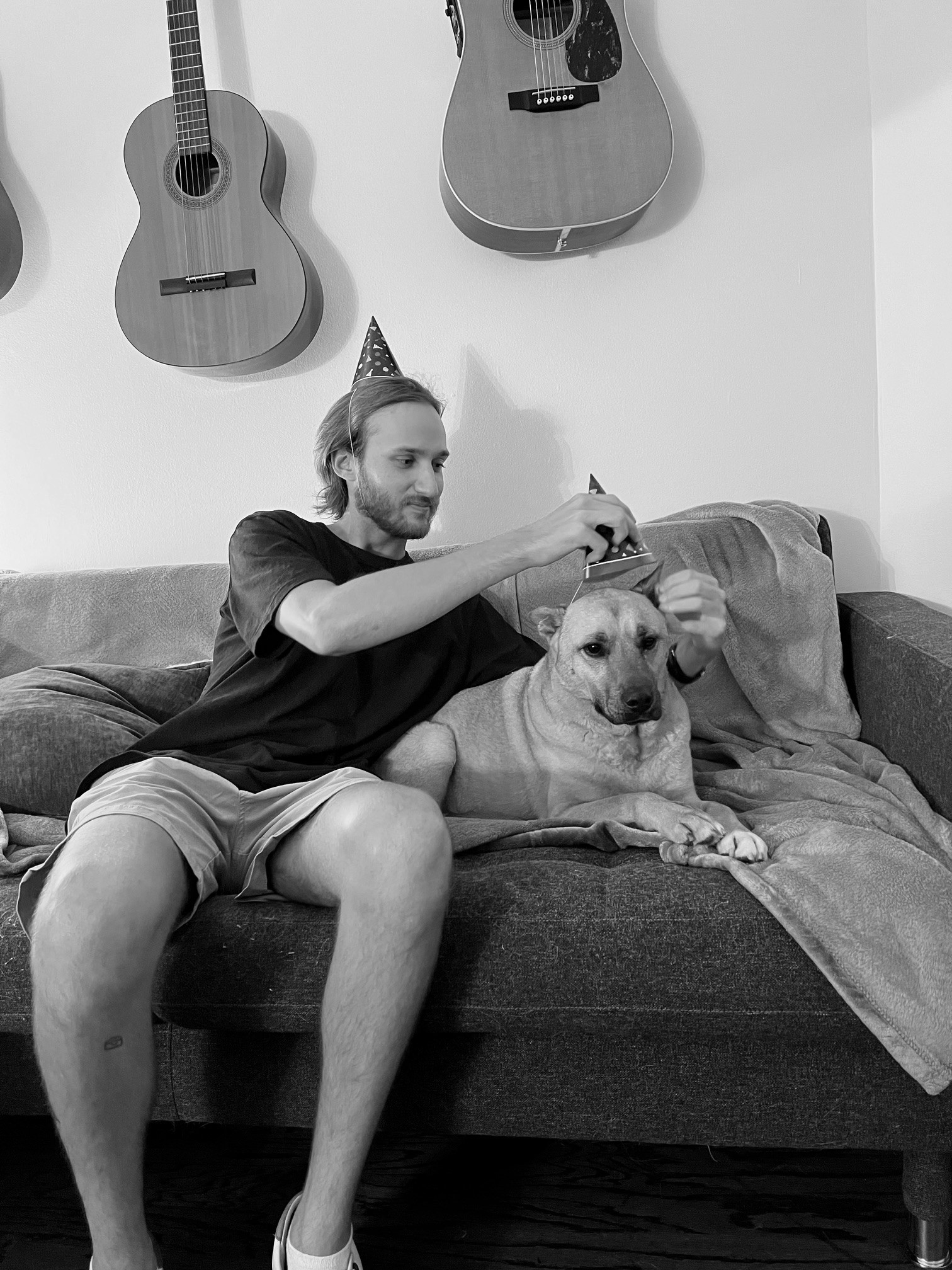 Man in a party hat putting a party hat on a dog