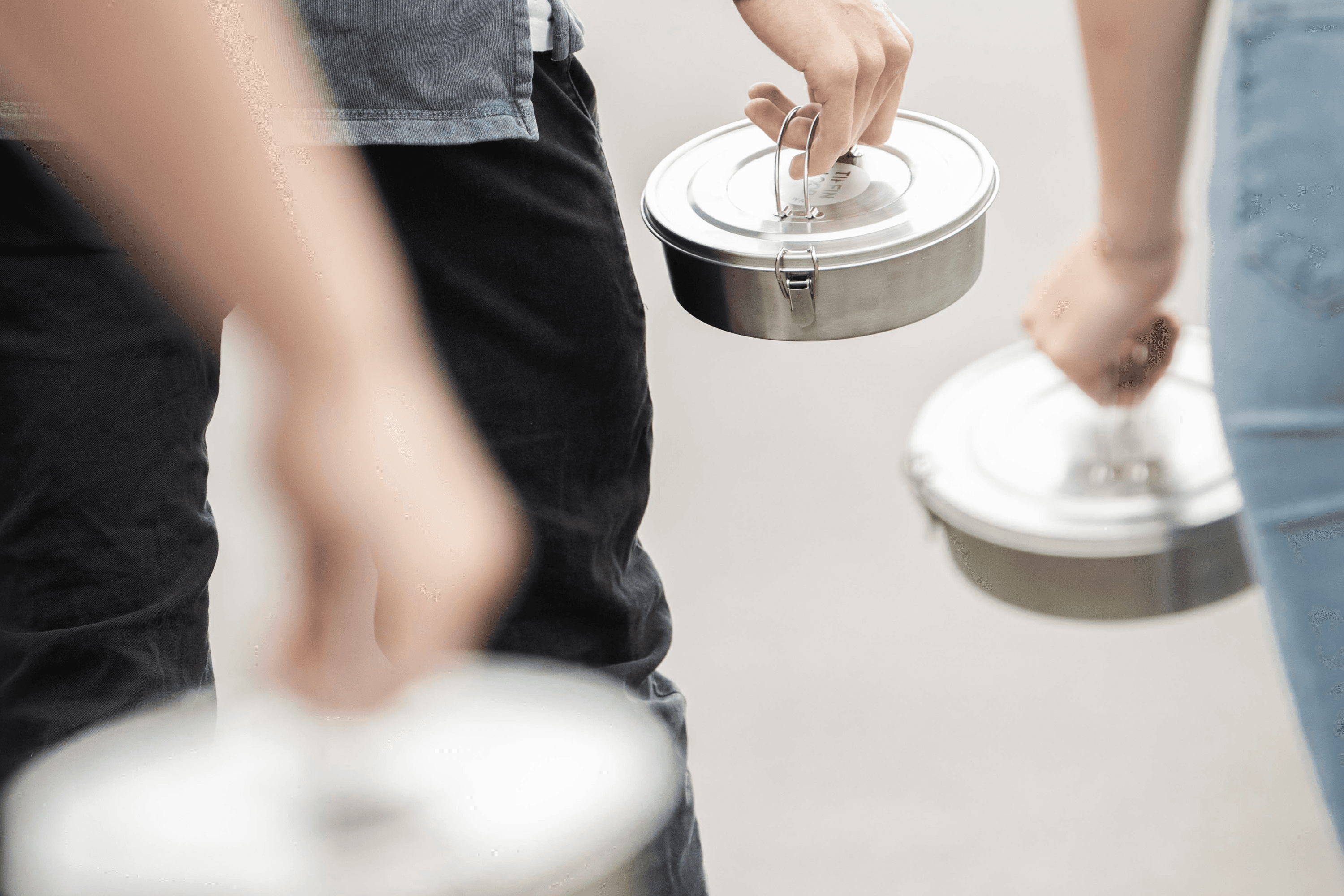 Two people carrying metal tiffin lunch containers.