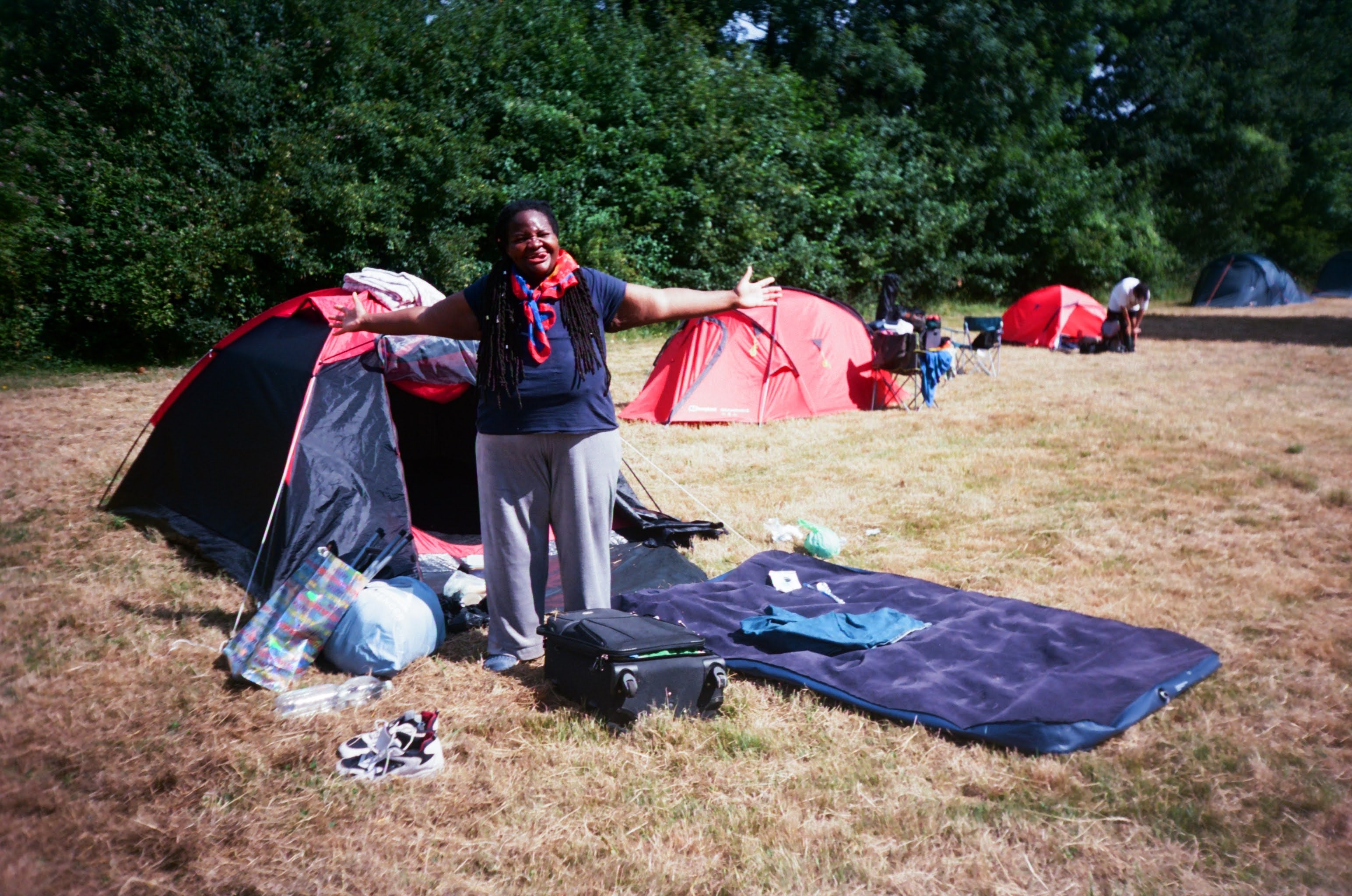 A person extends arms out wide and smiles outside a tent set up