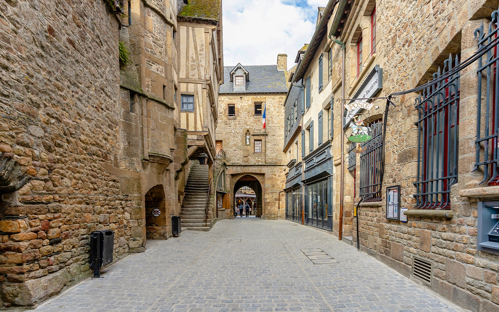 Narrow cobblestone street in Le Mont Saint Michel with historic stone buildings.