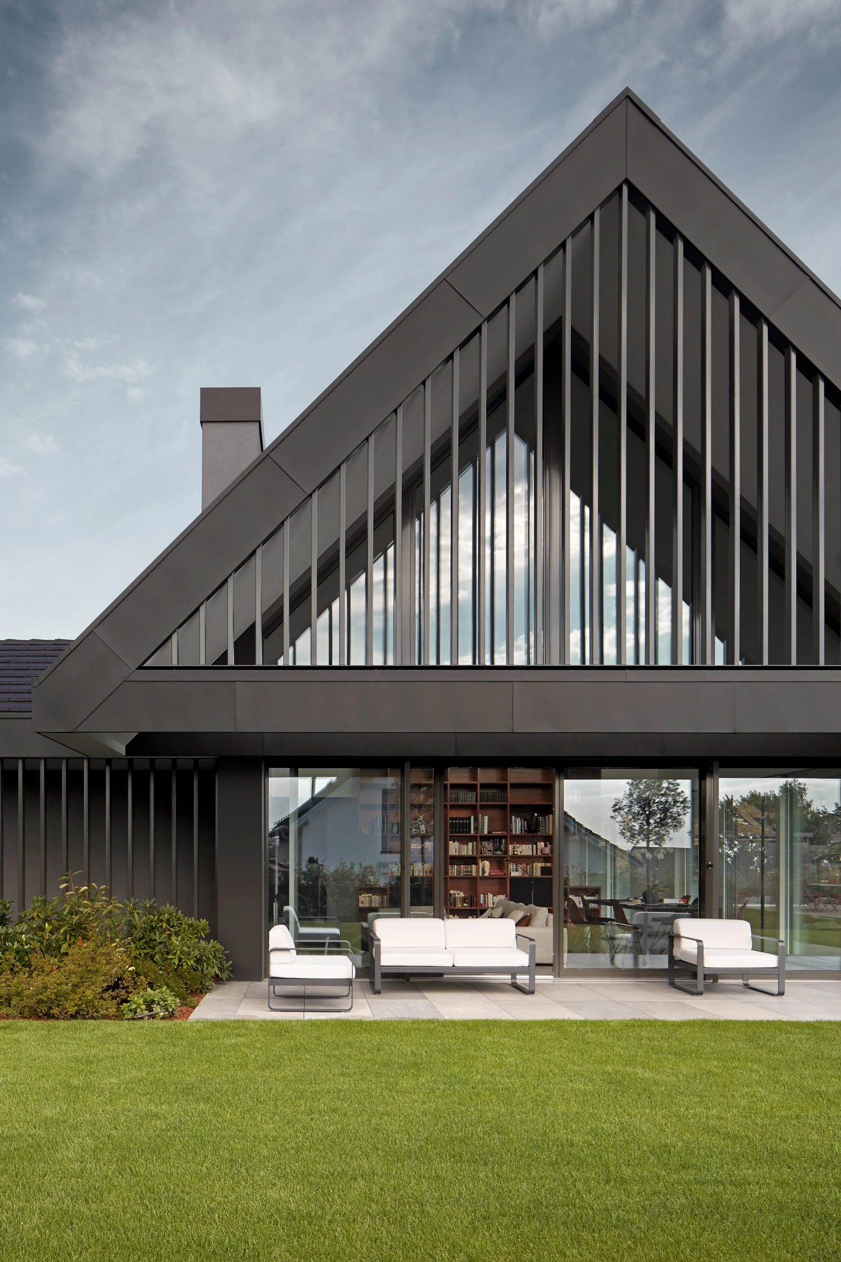 Détail de la façade de la maison contemporaine à Jouxtens-Mézery, avec espace extérieur couvert et bardage métallique noir au design moderne et épuré.