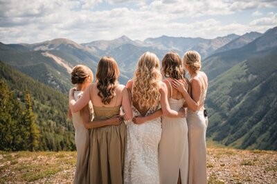 The bride and four bridesmaids stand arm in arm, facing the mountain valley.