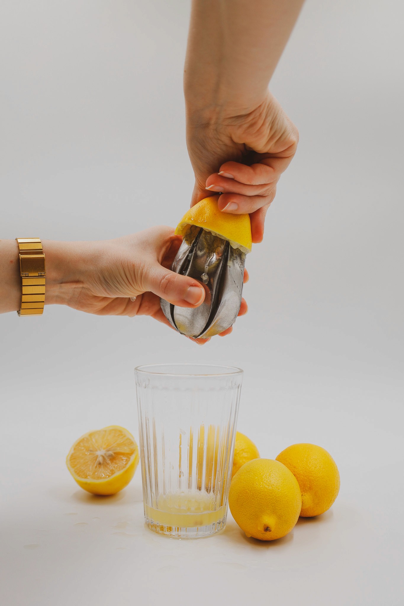 A hand squeezing a lemon half over a glass with several lemons on the table, extracting fresh lemon juice for a refreshing beverage.