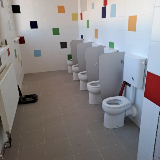 Dětská toaleta s několika záchody, bílými dlaždicemi a barevnými čtvercovými akcenty na stěnách.