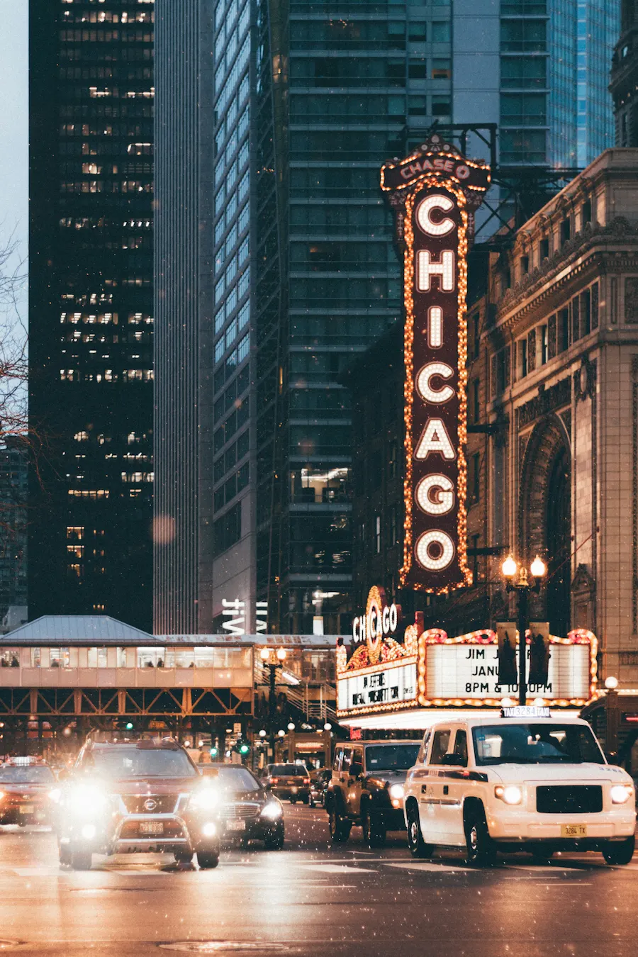 Chicago Theatre marquee glowing on State Street in downtown Chicago with evening traffic and city lights.