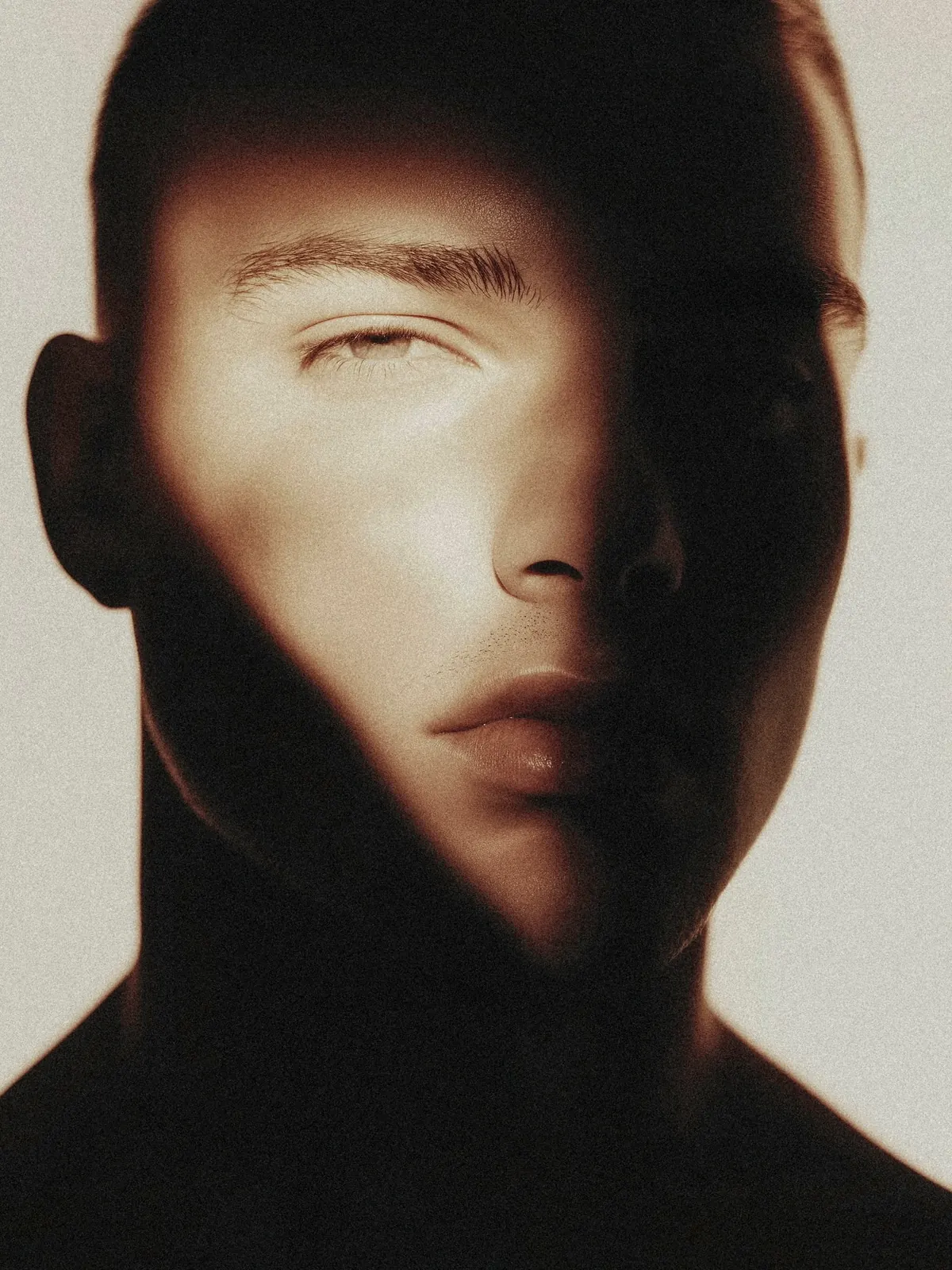 Close-up portrait with one eye closed and an angled beam of warm light across the face.