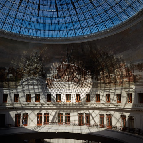 A glass-domed atrium with a large mural and multiple windows, casting intricate shadows on the walls.