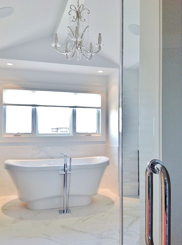 Image of Luxurious primary ensuite bathroom with freestanding tub, marble floor, and elegant chandelier by KHD Homes.
