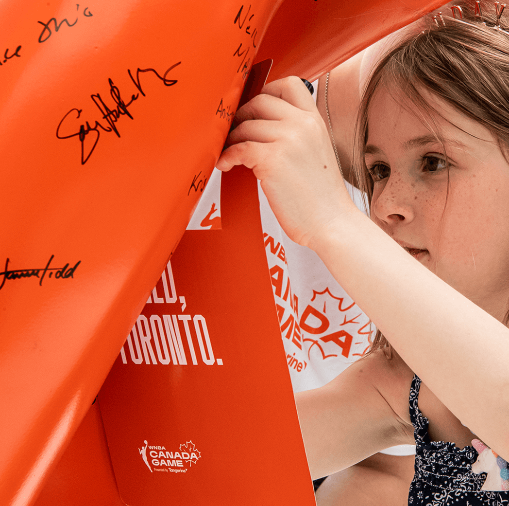 A child examines an orange banner covered in signatures, with a focused expression on their face.