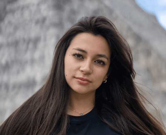 a young man wearing glasses standing in front of a mountain