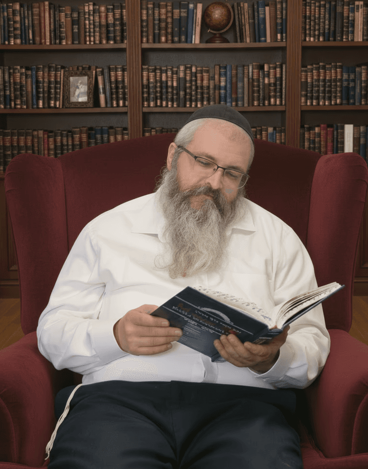 Smiling female therapist with short gray hair, wearing a brown top and a purple shawl, surrounded by a cozy background.