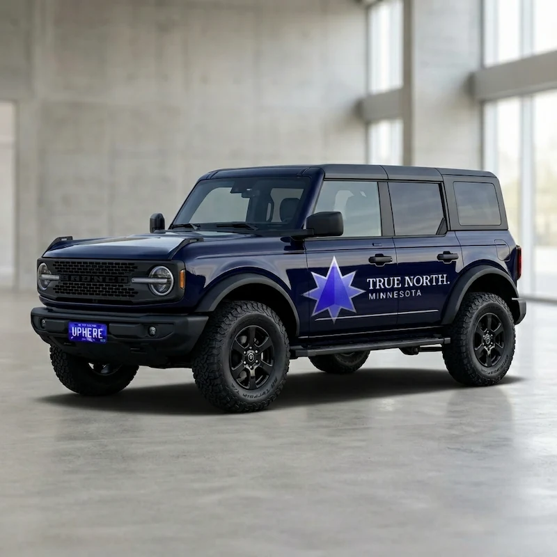 A deep navy Ford Bronco in an indoor studio setting with the True North. Minnesota logo applied as a large vehicle wrap graphic on the door panel, with the UPHERE license plate visible on the front.