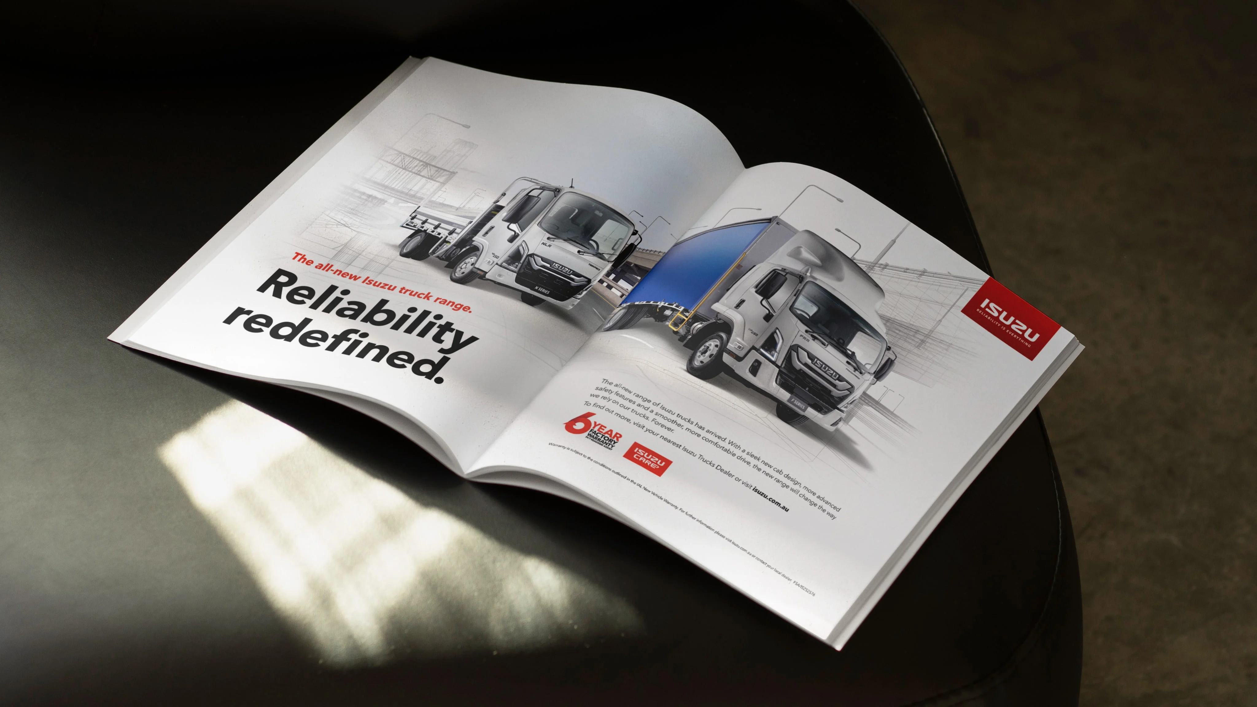 Open magazine spread of the all-new Isuzu truck range with the headline 'Reliability redefined.' on a dark surface