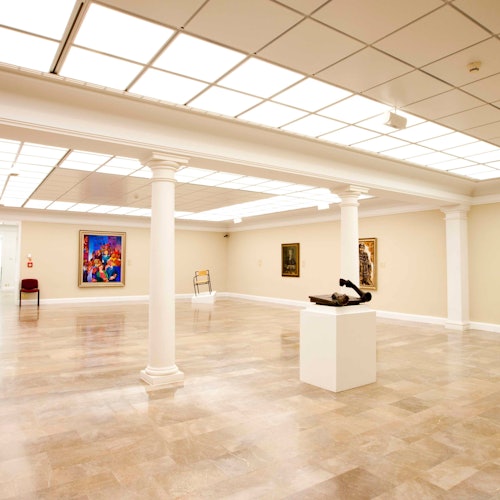寬敞的畫廊,擁有經過打磨的地板、柱子、牆上的現代藝術,前景中有一座放在基座上的雕塑。