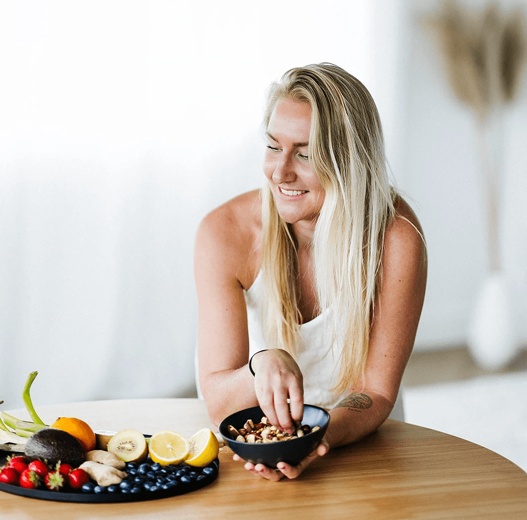 Daphne Medema van Hormone Healing Hub glimlachend aan tafel met vers fruit en noten, symbool voor hormonale balans door voeding.