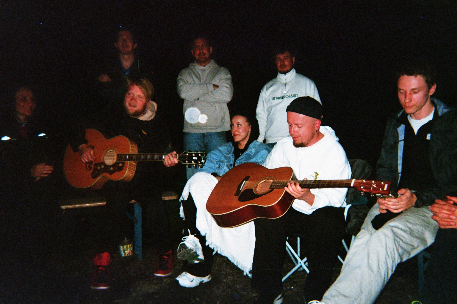 Junge Menschen sitzen zusammen vor dem Lagerfeuer, singen und spielen Gitarre.