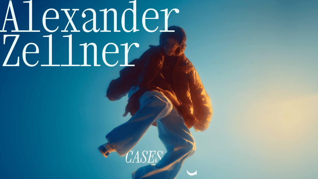 A person wearing headphones sits at a desk with a large curved monitor displaying graphic design software, surrounded by a laptop, smartphone, and potted plant, creating a modern workspace setup.