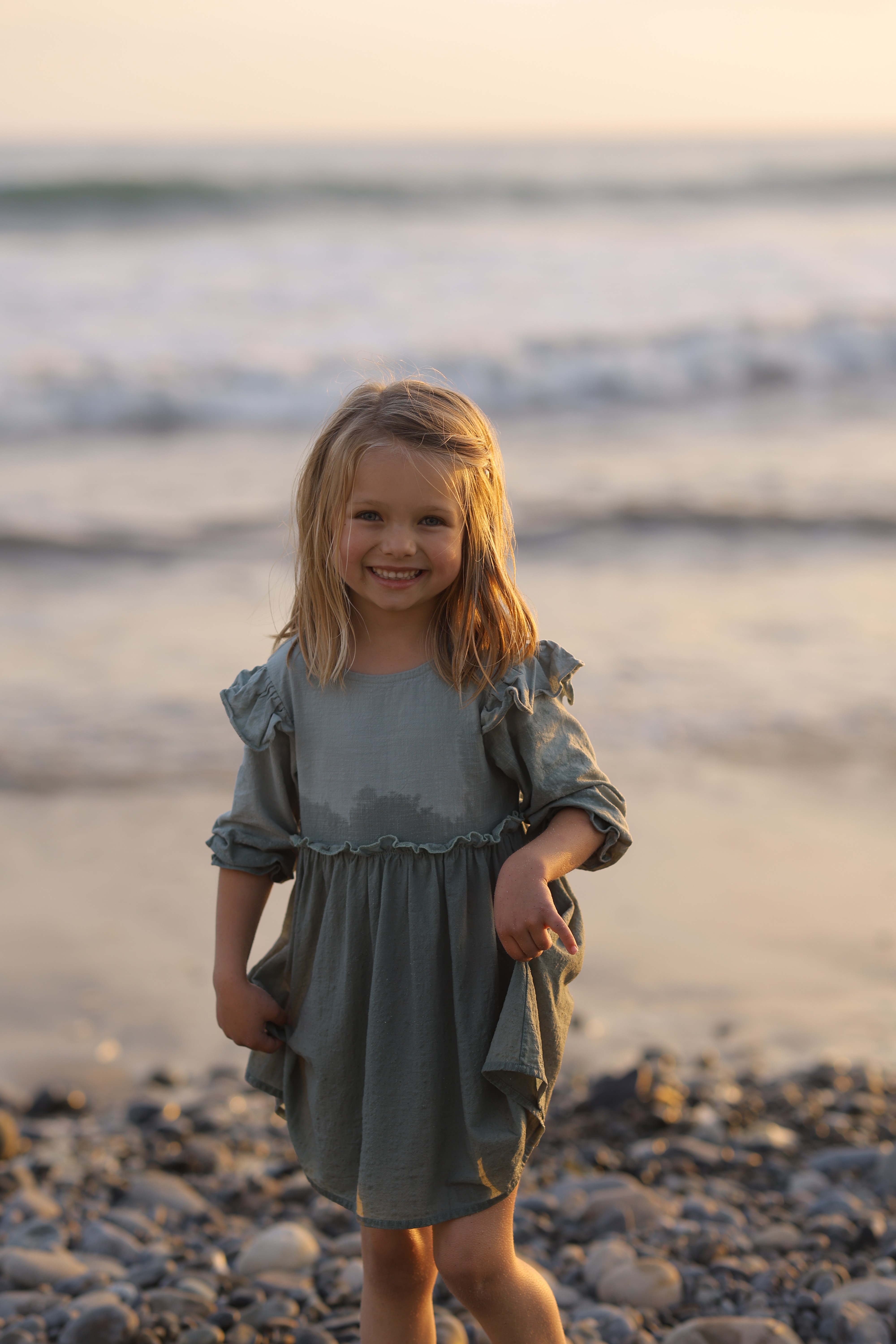 Little girl standing near the ocean at sunset during a warm, relaxed family photoshoot.