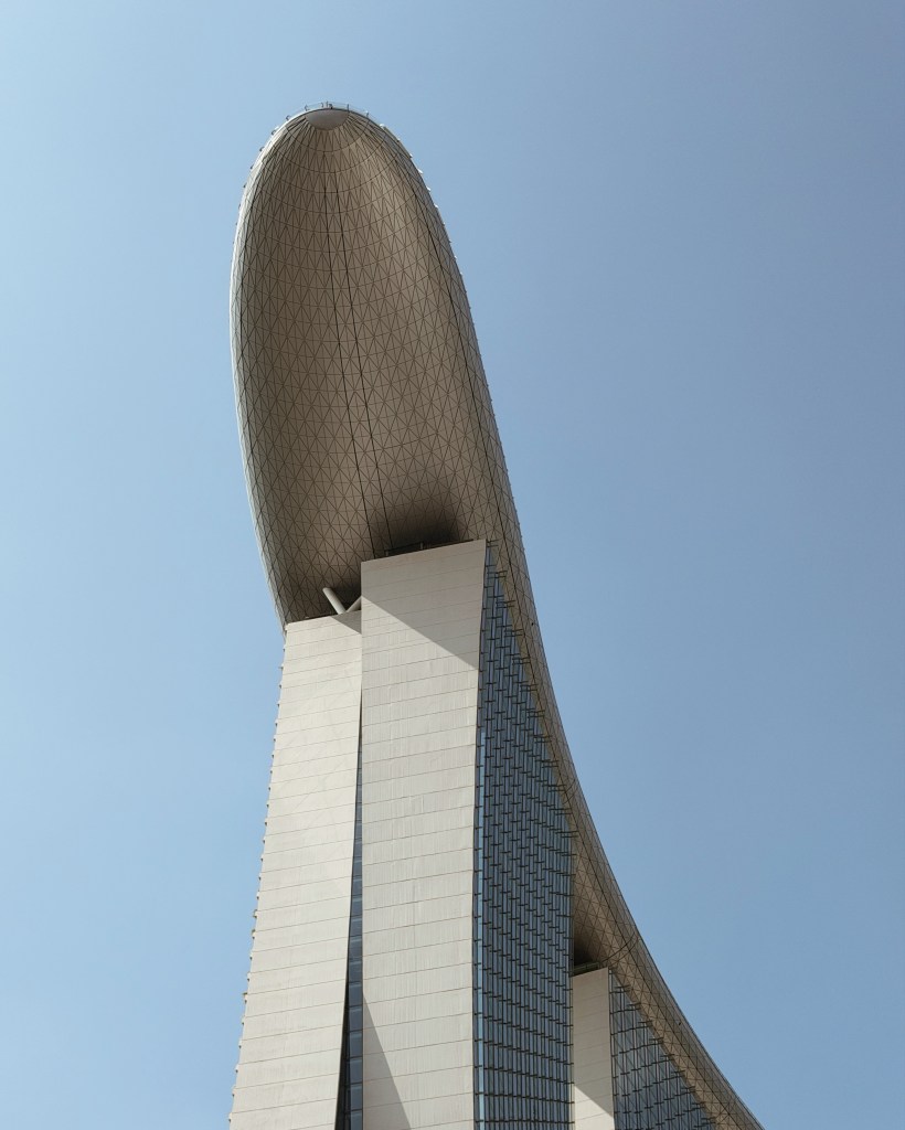A close-up view of a modern architectural building with a distinctive curved roof, set against a clear blue sky.