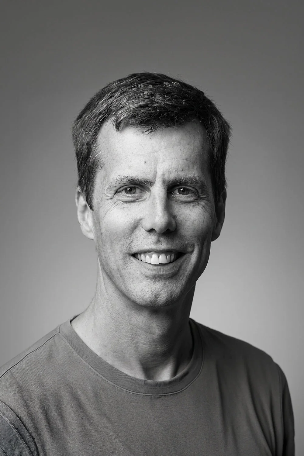 A smiling man, with soft lighting and a professional backdrop.