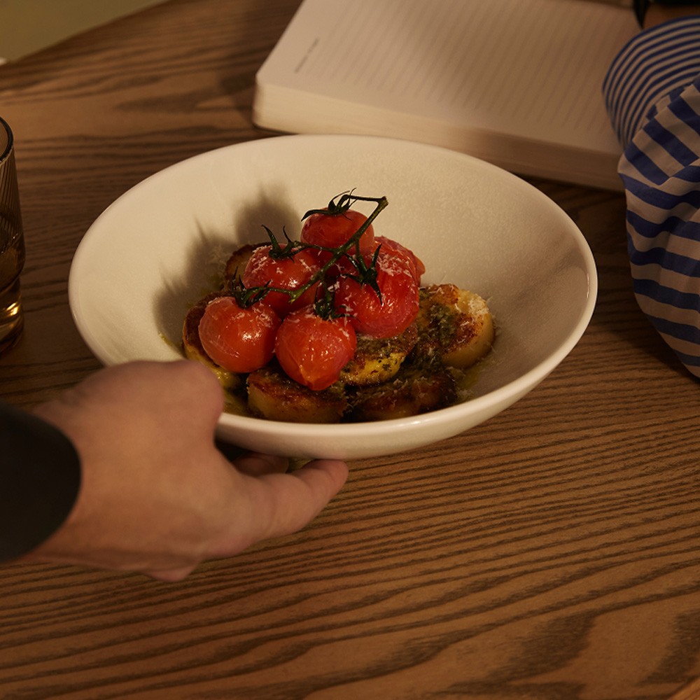Hand placing a bowl of roasted cherry tomatoes and toasted bread on a table setting.