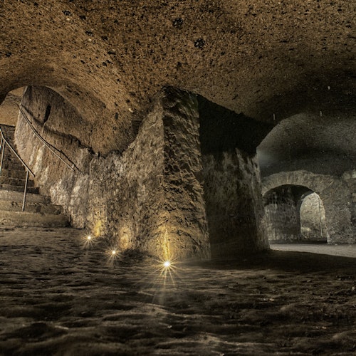 微弱灯光照明的石墙地下隧道，拥有拱形天花板、台阶以及沿途的微光。