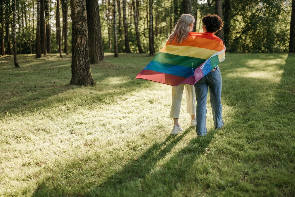 Two femmes walking with a pride flag in a forest.