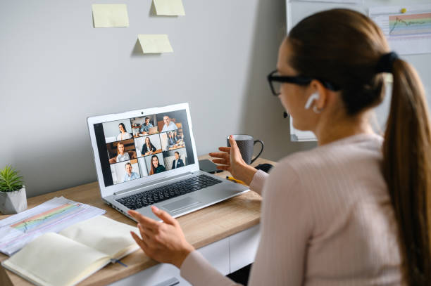 Professionista in smart working durante videoriunione su laptop, home office organizzato con appunti e grafici.