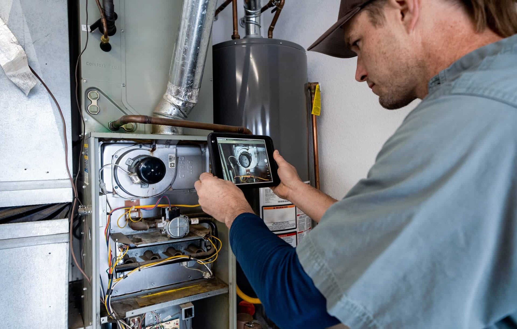 Professional HVAC technician inspecting the inside of a furnace with a flashlight.