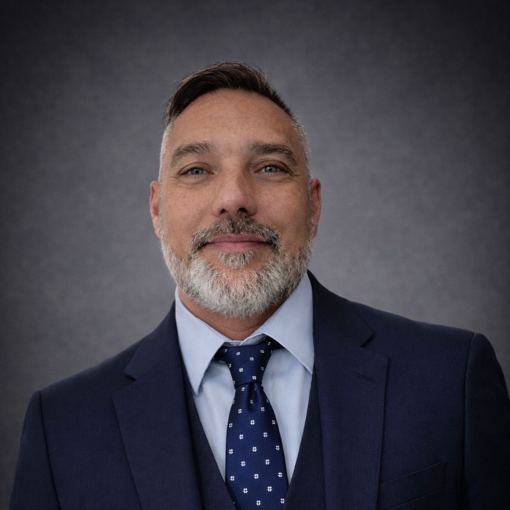 Professional headshot of a woman with short, wavy brown hair wearing a black blazer and white shirt.
