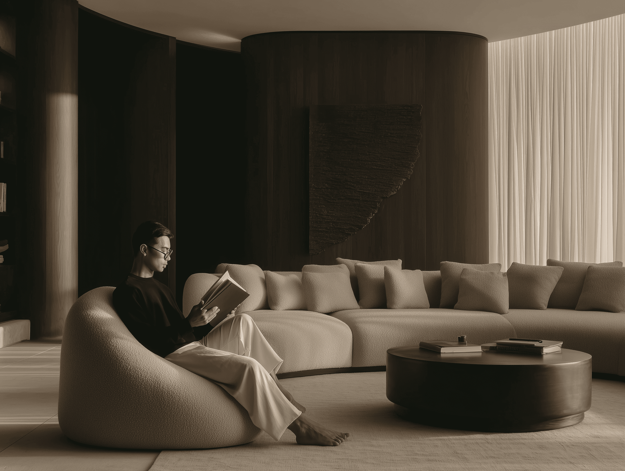 A man reading in a sculptural boucle lounge chair within a darkly moody interior featuring a curved dark timber column, cream curved sofa, and sheer floor-to-ceiling drapes